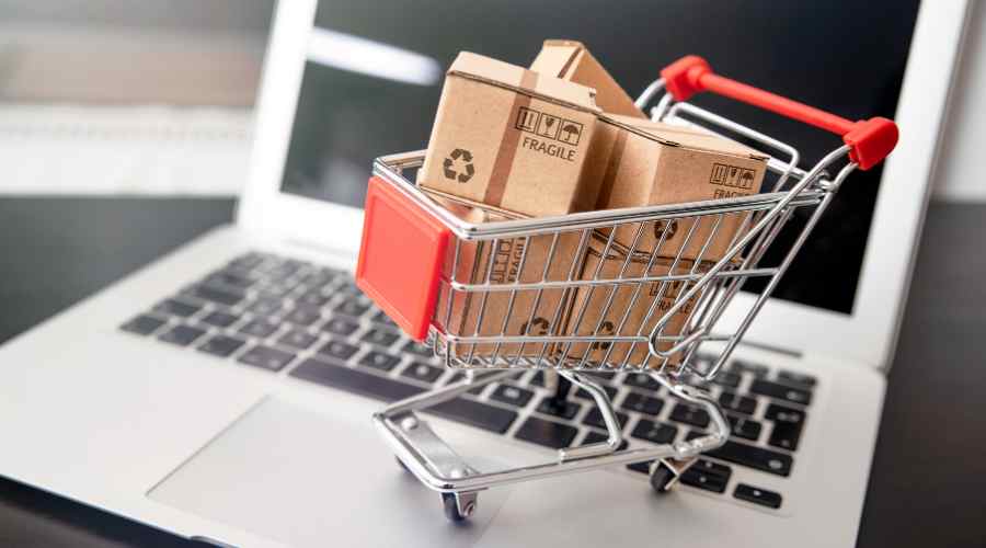 A small shopping trolley filled with tiny packages stands on an open laptop