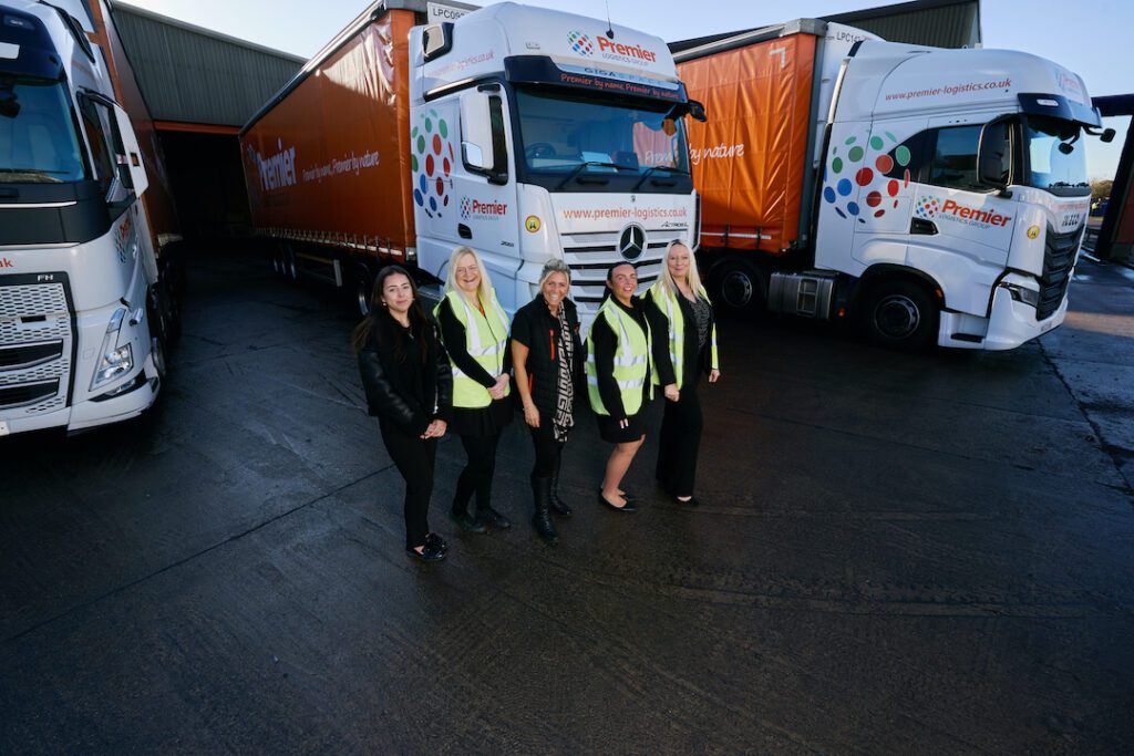a high wide angle shot of four women in high vis jackets in front of Premier Logistics trucks in Leicester