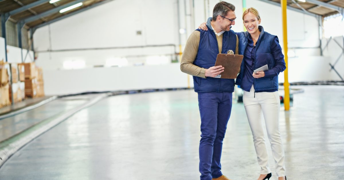 Comparing their inventory lists. Shot of two coworkers talking while standing in a large warehouse | Choosing the Right Warehouse Solutions for Your Business