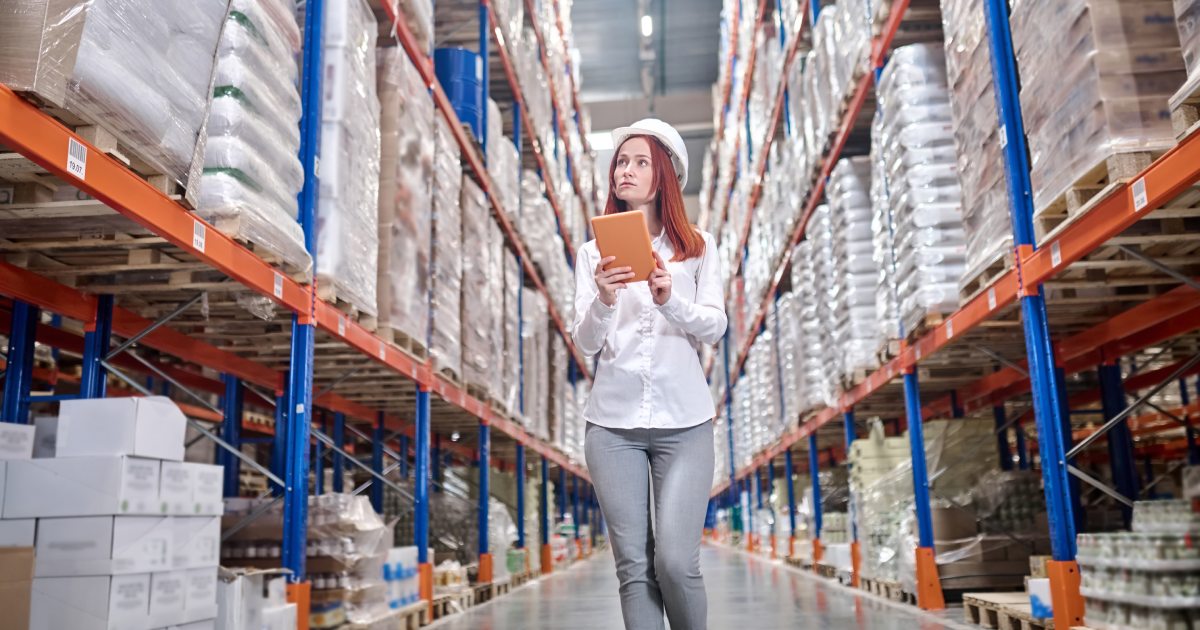Woman with tablet looking attentively at shelves in warehouse | The Impact of Proper Inventory Management on Your Fulfilment Operations