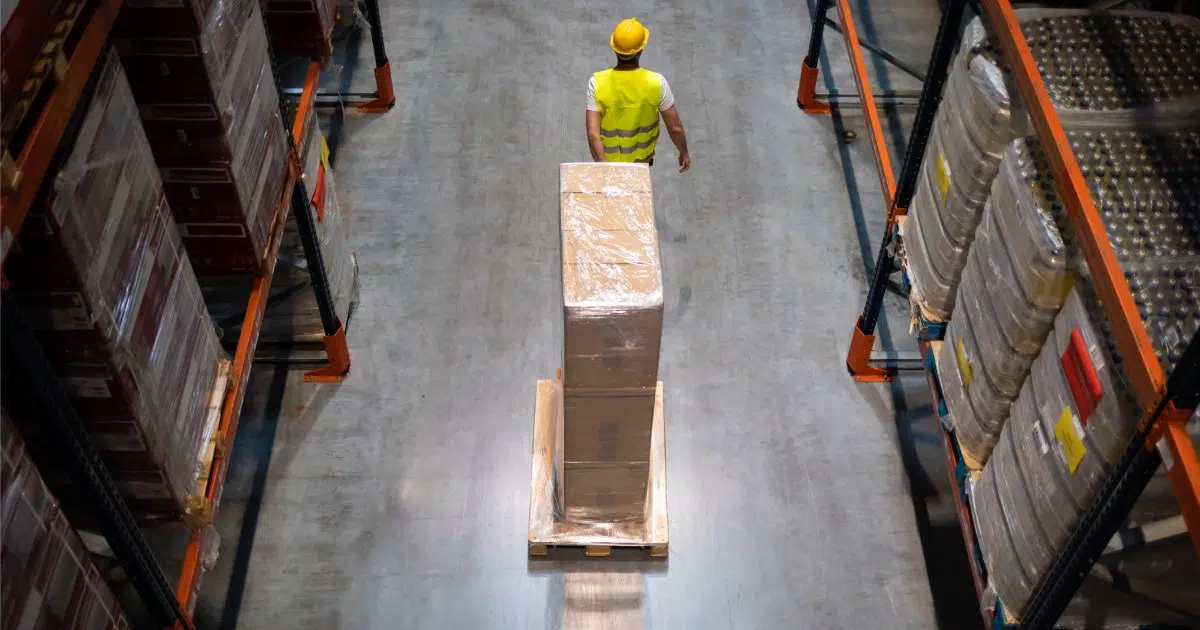 Warehouse worker pulling a pallet truck between shelves, above view | Logistics Industry in the UK