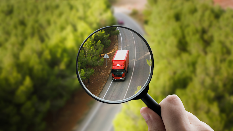 magnifying glass over a red truck on a road between the trees